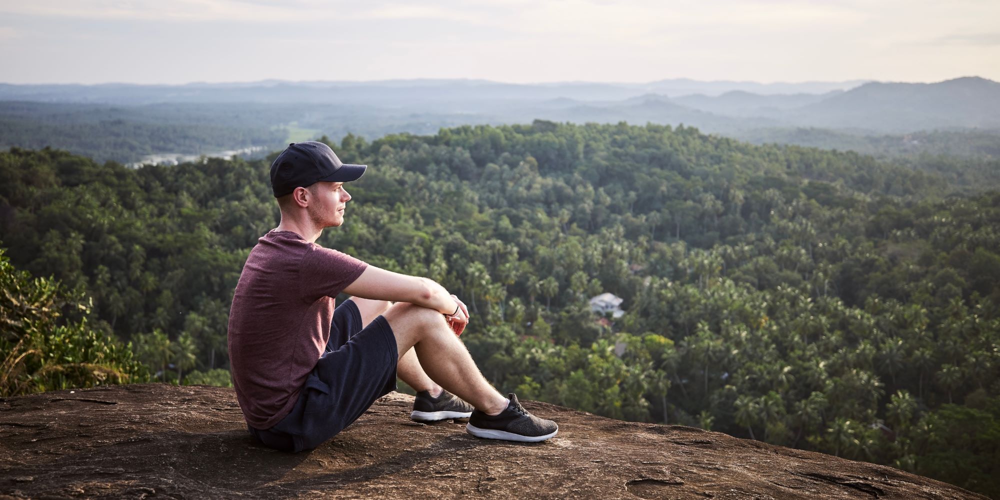 Joven en una colina, mirando hacia el horizonte. Usa ropa deportiva. Está descansando activamente.